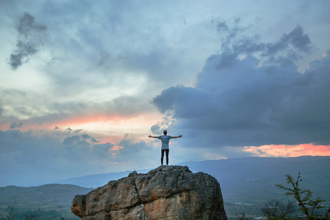 A person standing on a mountain summit with arms open to the sunset